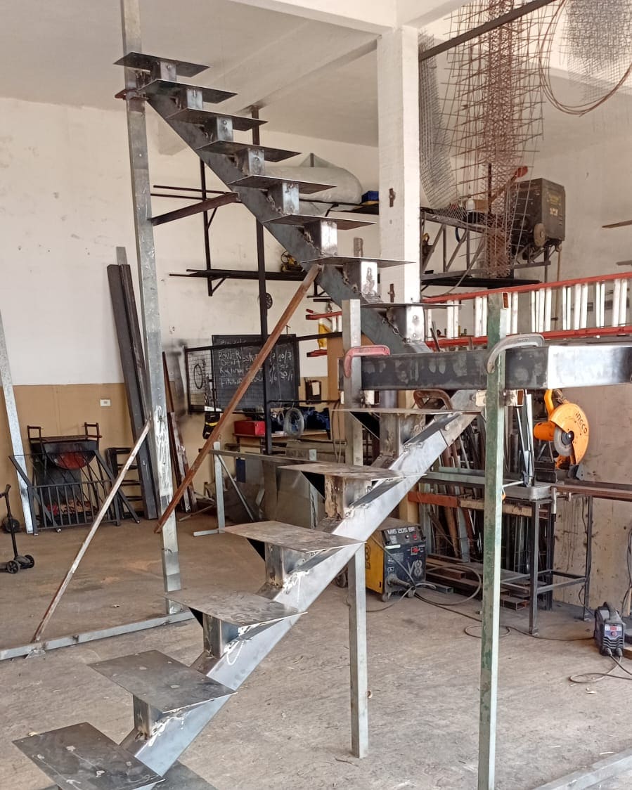Escada metálica em L em fabricação na oficina da Serralheria RPS, com equipamentos ao fundo