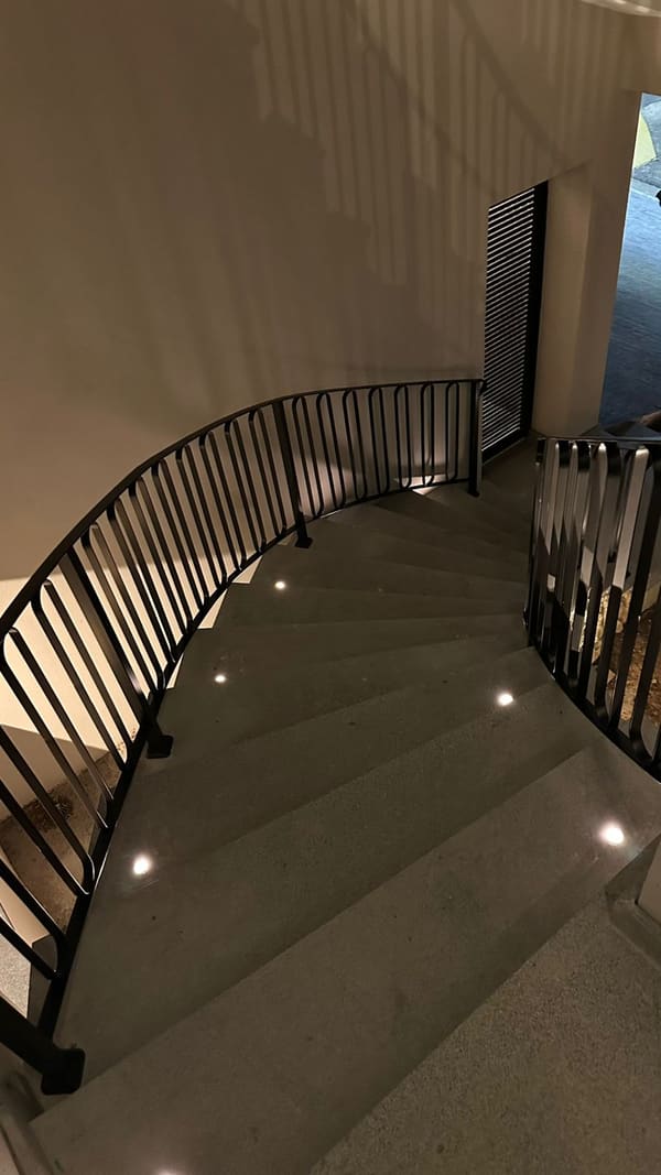 Corrimão e guarda-corpo metálicos pretos acompanhando uma escada curva na entrada de uma casa